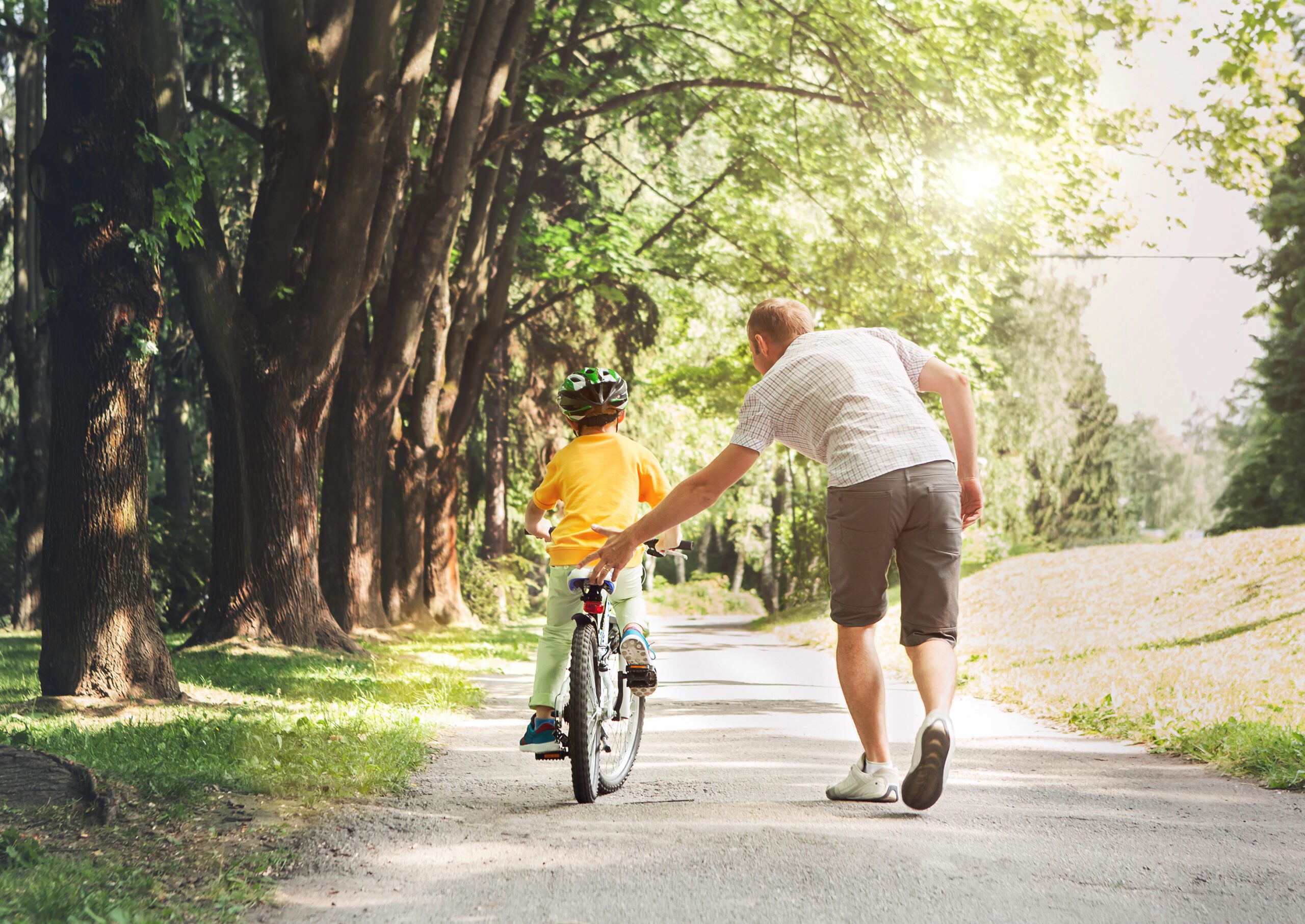 Adult helping boy learn to ride a bicycle