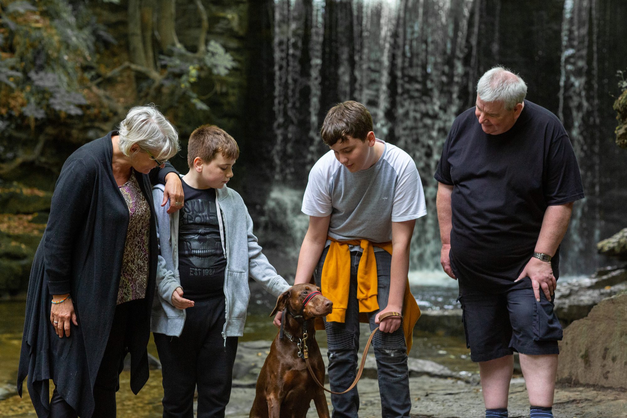 Ellen and Paul, foster carers with two teenagers and a dog in front of a waterfall